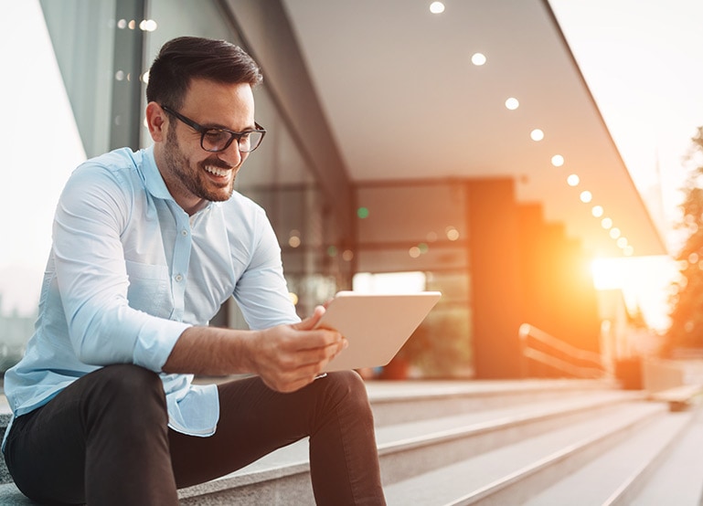 A man is smiling while looking at his tablet.